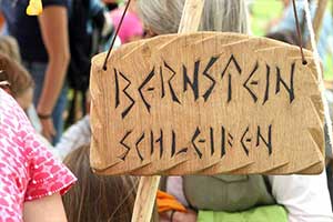Holzschild mit der Aufschrift 'Bernstein schleifen' bei einem Familienfest